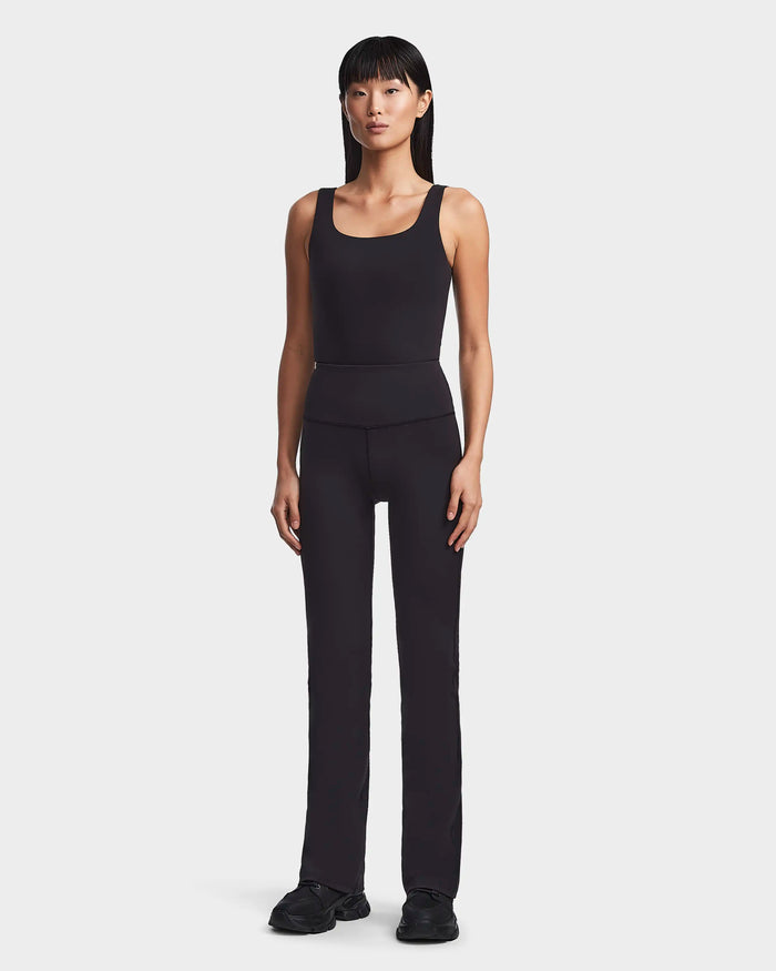 A person with straight, shoulder-length hair and a neutral expression stands against a plain background, wearing the ADRIANA - 8523550 Black sleeveless top and high-waisted flared pants by Rudsak, paired with black shoes.