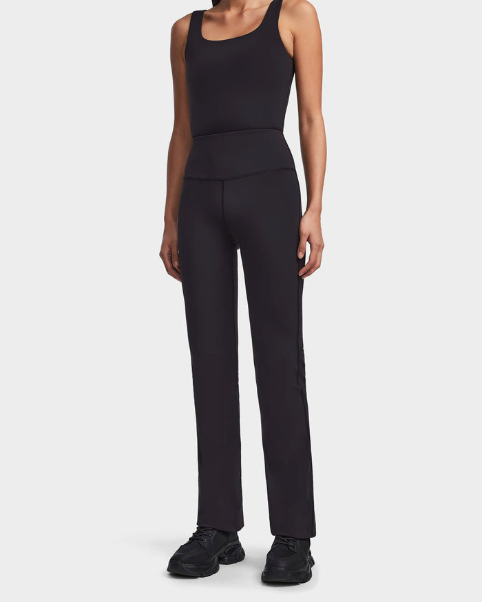 A person wearing Rudsak's ADRIANA - 8523550 Black sleeveless fitted tank top and high-waisted black flare pants with black athletic shoes, standing against a plain white background.