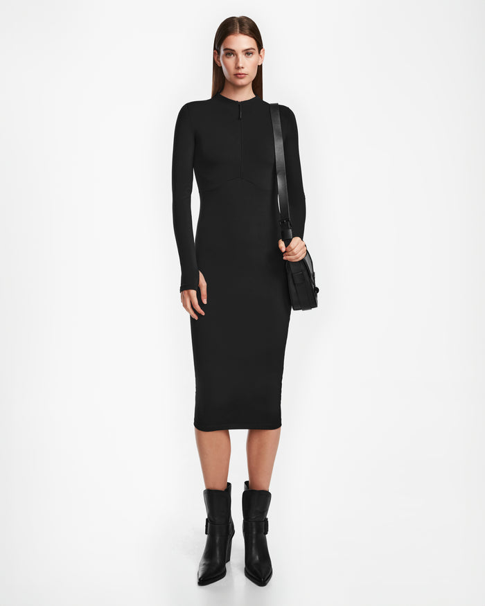 A woman faces forward wearing the Rudsak AGNES - 8524551 Black bodycon stretch dress with black ankle boots and a shoulder bag against a plain white background.
