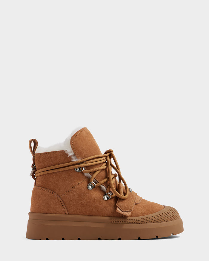 The Rudsak ALEXEY - L225025 Tan is a women’s suede winter boot with a flat rubber sole for traction, tan laces, metal eyelets, and plush wool lining, shown on a plain light background.