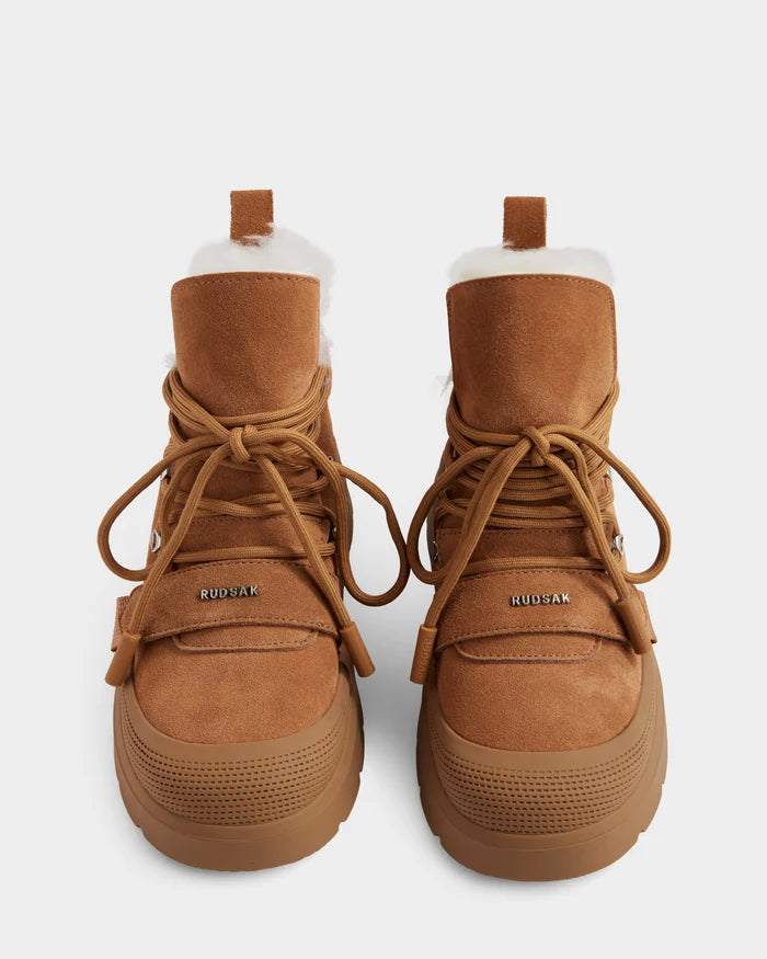 The Rudsak ALEXEY - L225025 Tan women’s suede winter boots feature thick rubber soles, large brown laces, and plush faux fur lining. Shown from above on a white background with the Rudsak logo visible on the front.