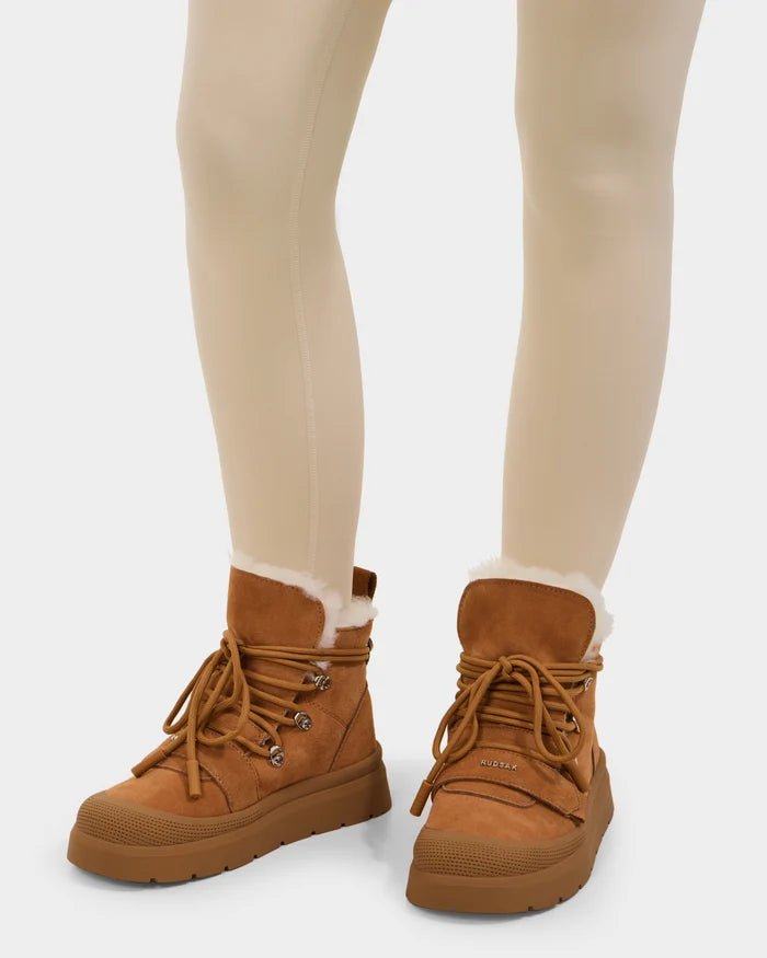 A person wearing cream-colored leggings and Rudsak ALEXEY - L225025 Tan women’s suede winter boots with a rubber sole and cozy wool lining, standing on a white background.