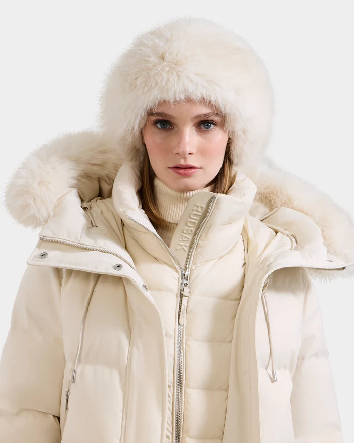 A woman in the Rudsak ARLETTE - 8425544 Vanilla cream puffer jacket with a fur-lined hood, paired with a faux fur headband and light turtleneck, looks at the camera against a plain light background.