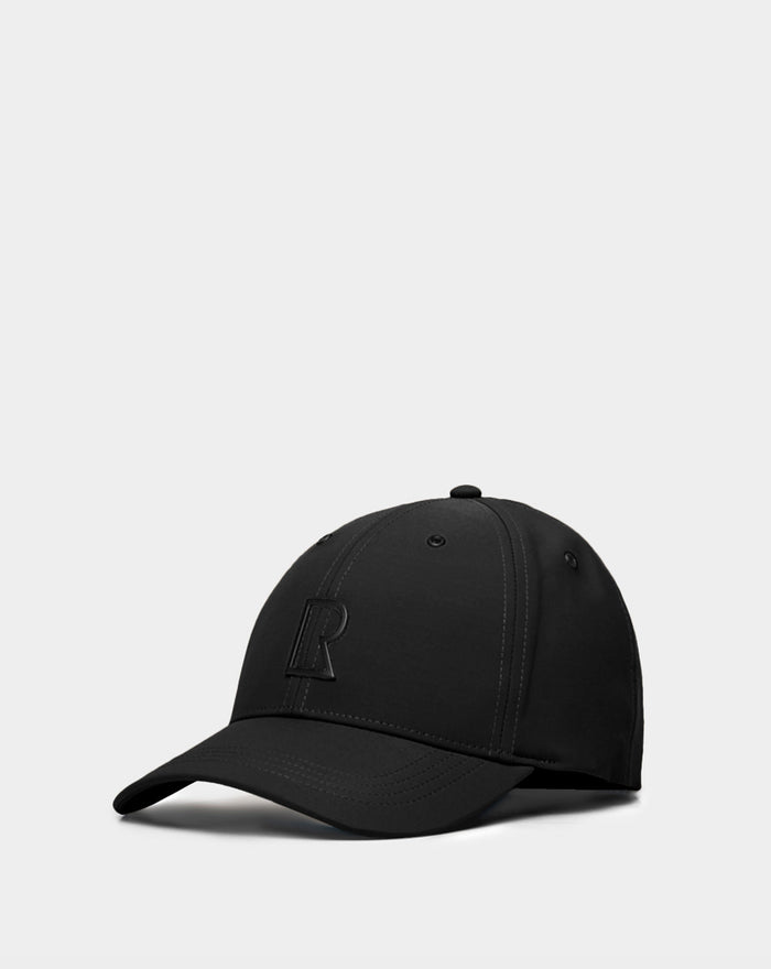 The ARSENE - 9422504 Black by Rudsak is a black unisex baseball cap featuring subtle stitching and a raised letter R on the front, shown against a light gray background. This adjustable cap combines style and comfort for daily wear.