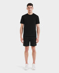 A man faces forward wearing the Rudsak ASHER - M525000 Black tailored-fit mens cotton t-shirt with a minimalist chest logo, paired with black shorts and white sneakers, set against a plain white background.