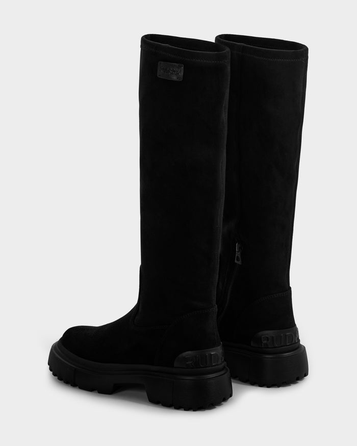 The AVOLA - L225514 Black by Rudsak are tall women’s knee-high faux-suede boots with chunky rubber soles, side zippers, and a subtle raised heel logo, shown against a plain light gray background.