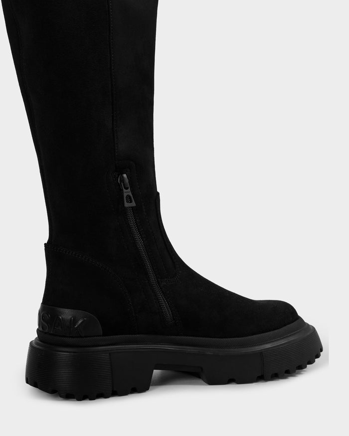 A close-up of the AVOLA - L225514 Black knee-high boot by Rudsak, featuring a chunky sole, side zipper, and embossed branding on the heel, shown against a plain light background.