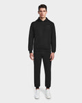 A man faces forward wearing the Rudsak BARRY - 9524011 Black M oversized unisex hoodie with matching jogger pants and white sneakers, set against a plain white background.