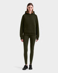 A woman stands facing forward wearing the Rudsak BARRY - 9524011 Dark Olive W hoodie and matching leggings with black sneakers against a plain light background.