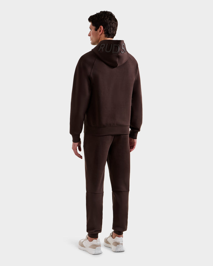 A man faces away, wearing the BARRY - 9524011 Espresso M hoodie and joggers from Rudsak with "RUDDS" on the hood, paired with white sneakers, all set against a plain light gray background.