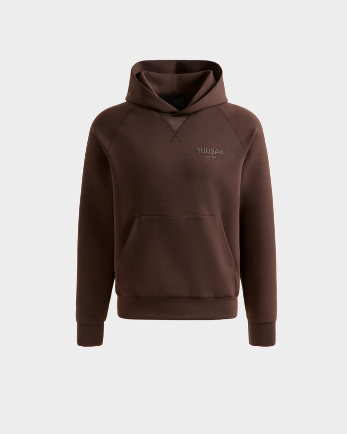The Rudsak BARRY - 9524011 Espresso M is a brown unisex oversized hoodie with long sleeves, a kangaroo pocket, and subtle RUDSAK branding on the left chest, shown against a plain light gray background.