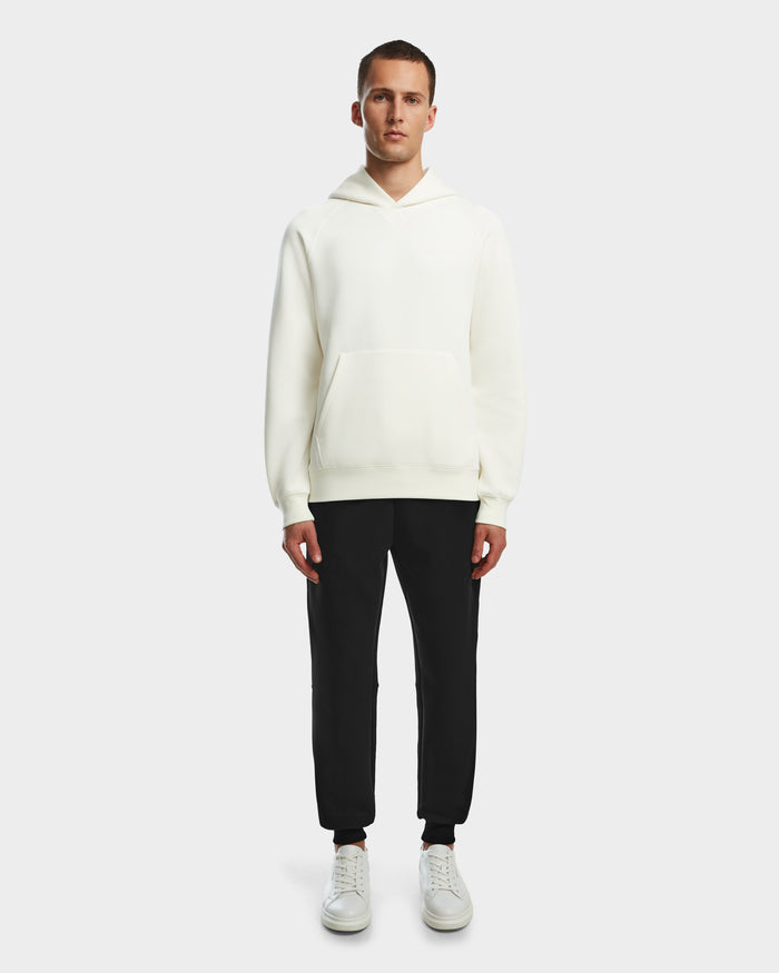 A man stands facing forward wearing the Rudsak BARRY - 9524011 Iceland M unisex oversized hoodie, paired with black pants and white sneakers, against a plain light gray background.