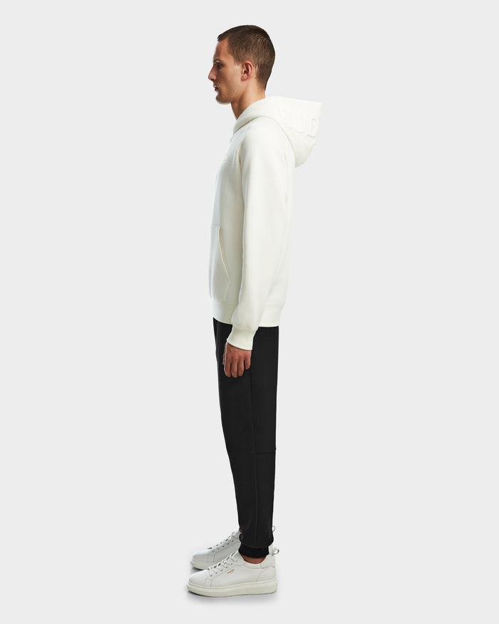 A man stands in profile facing left, wearing the Rudsak BARRY - 9524011 Iceland M hoodie with a unisex fit, paired with black pants and white sneakers against a plain light gray background.
