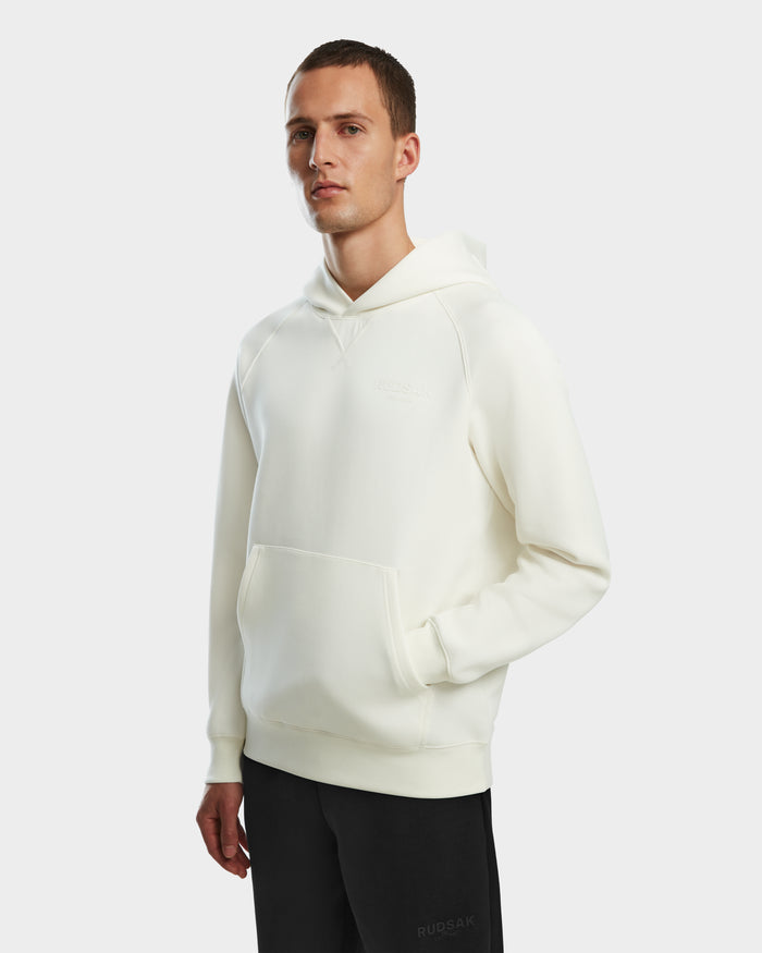 A man wearing the Rudsak BARRY - 9524011 Iceland M unisex white hoodie with a front pocket stands against a white background, looking at the camera with one hand in his pocket.