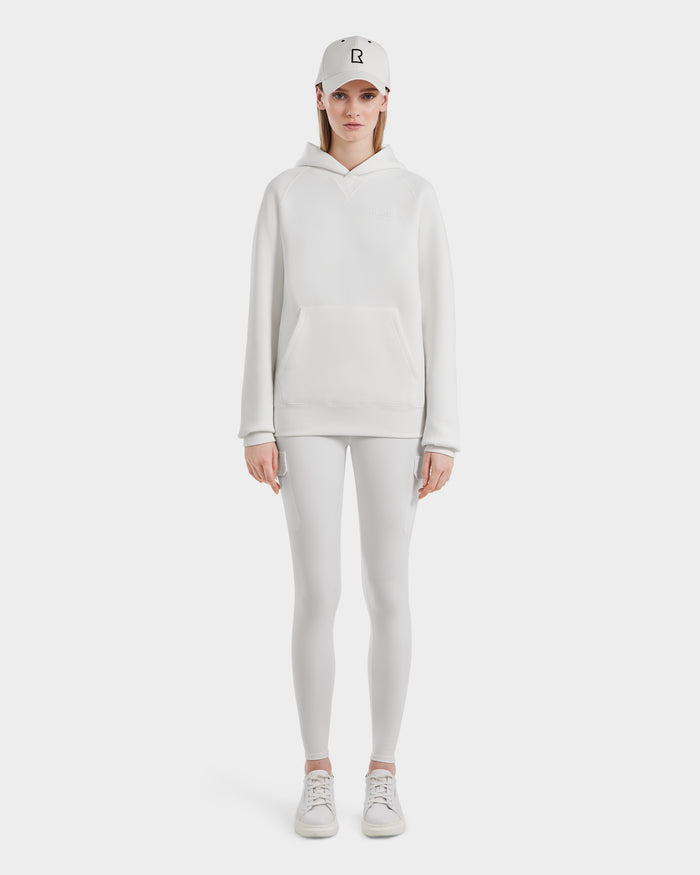 A person stands facing forward in the Rudsak BARRY - 9524011 Iceland W hoodie, paired with leggings, sneakers, and a baseball cap—an effortlessly cool look against a plain white background.