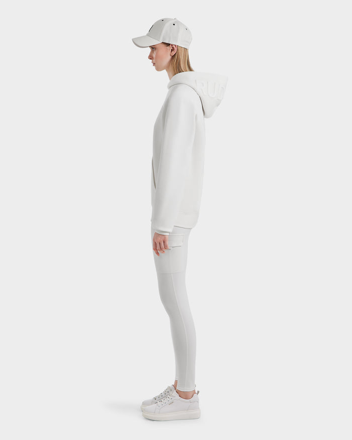 A person in profile wears the Rudsak BARRY - 9524011 Iceland W white oversized hoodie with hood down, styled with white leggings, sneakers, and cap against a plain white background.