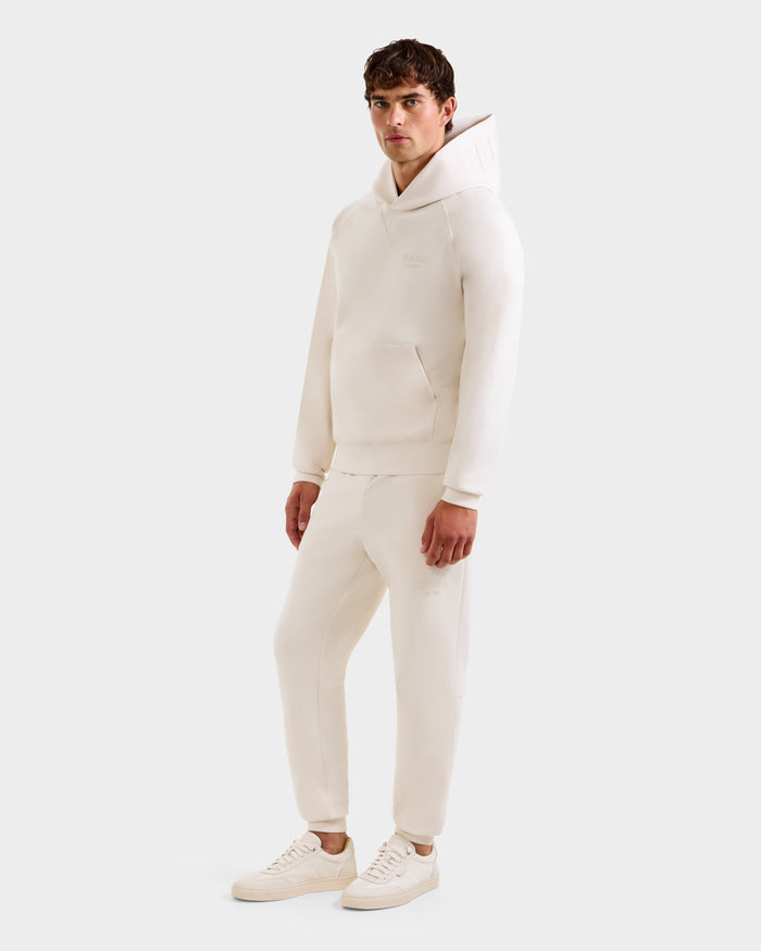 A man faces forward against a white background, wearing the Rudsak BARRY - 9524011 Vanilla M hoodie and matching sweatpants, paired with light sneakers.