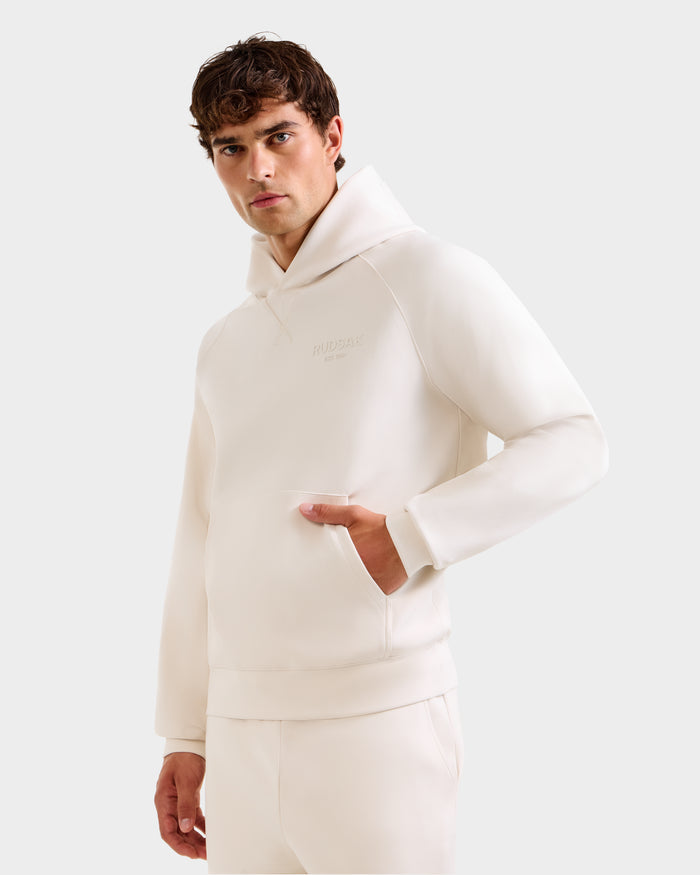 A young man with short brown hair confidently models the Rudsak BARRY - 9524011 Vanilla M hoodie and matching pants, standing with one hand in his pocket against a plain light background.