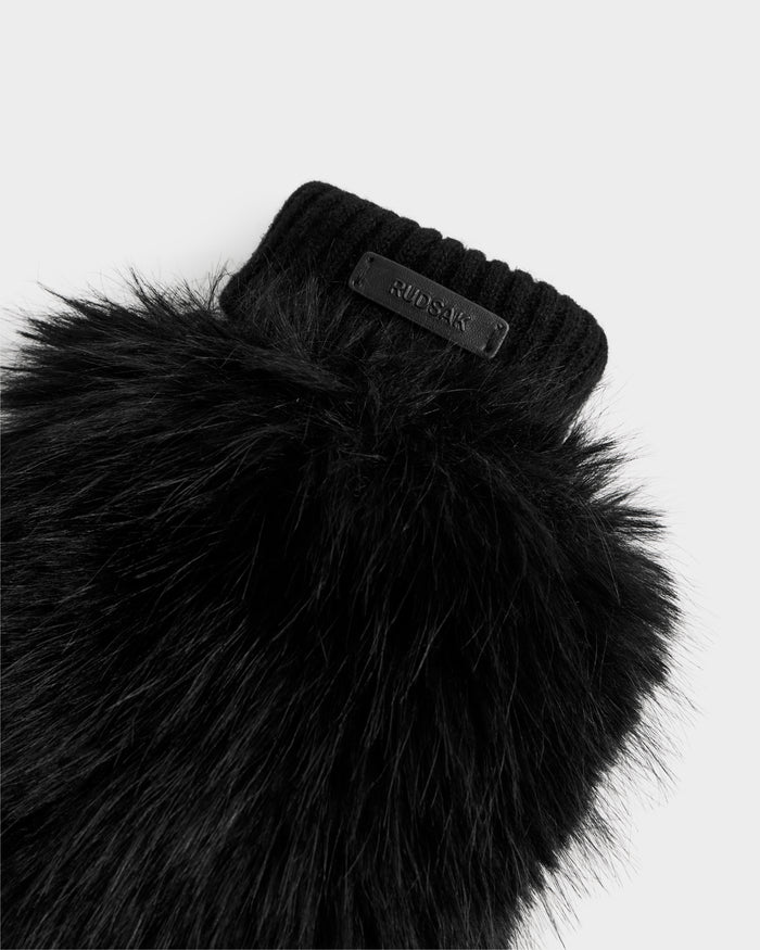 A close-up of the BELLA - 8425006 Black mitten by Rudsak, featuring black faux fur, a ribbed cuff, and a small rectangular logo label, photographed against a plain white background.