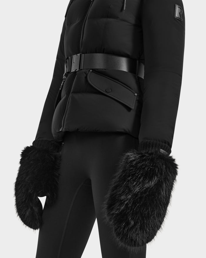 A person wears the Rudsak BELLA - 8425006 Black belted puffer jacket with black leggings and oversized faux fur mittens—an ideal winter look—shown from shoulders to thighs against a plain background.