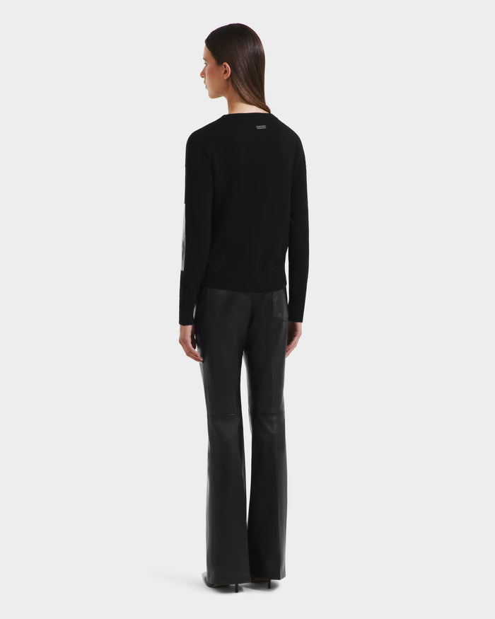 A person faces away, wearing the Rudsak BELLEROSE - 8525554 Black crewneck sweater and black leather flared pants against a plain light backdrop.