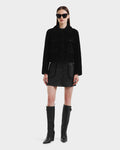 A woman faces forward against a white background, wearing the Rudsak BLAIR - 8125513 Black modern jacket, paired with a black mini skirt, tall black boots, and oversized black sunglasses.
