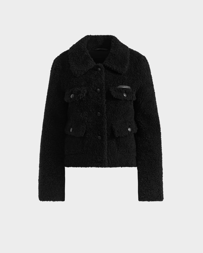 The Rudsak BLAIR - 8125513 Black is a women’s cropped teddy jacket featuring long sleeves, a collar, button-up front, and multiple flap pockets, shown on a plain white background for a sleek modern style.