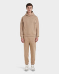 A man stands facing forward in the Rudsak BRIAR - 9525001 Almond M unisex hoodie and sweatpants set, made from a premium cotton blend, paired with white sneakers against a plain white background.