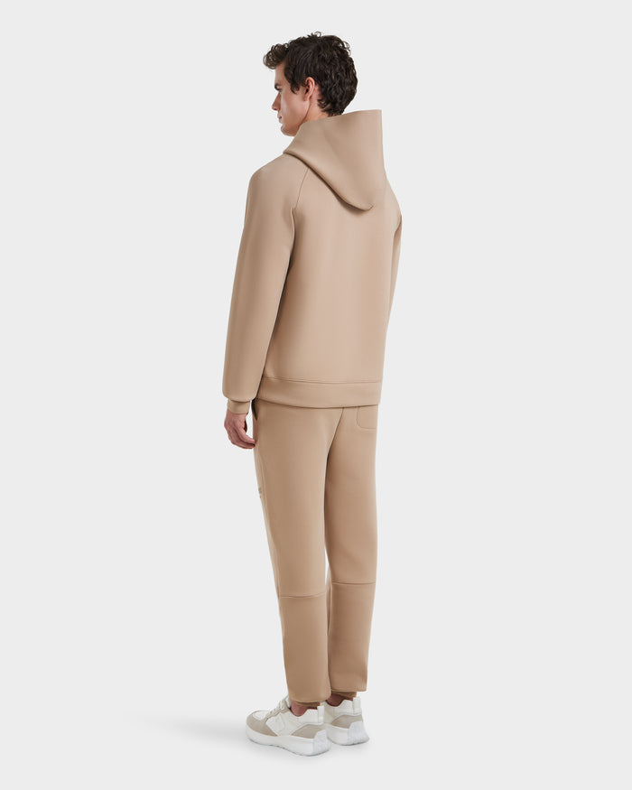 A person stands facing away, wearing the Rudsak BRIAR - 9525001 Almond M hoodie and jogger set, paired with white sneakers against a plain white background.