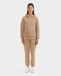 A woman faces forward in the Rudsak BRIAR - 9525001 Almond W beige premium cotton blend unisex hoodie and matching sweatpants, paired with white sneakers against a plain white background.
