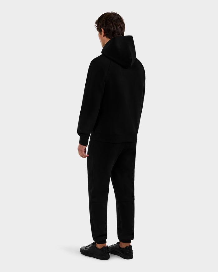 A person faces away from the camera wearing a Rudsak BRIAR - 9525001 Black M hoodie, paired with black sweatpants and sneakers against a plain light gray background.