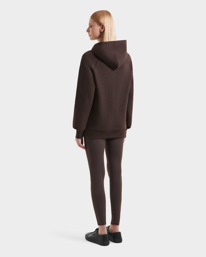 A person with long blonde hair is seen from behind wearing the Rudsak BRIAR - 9525001 Espresso W premium cotton blend hoodie, matching leggings, and black shoes against a plain white background.