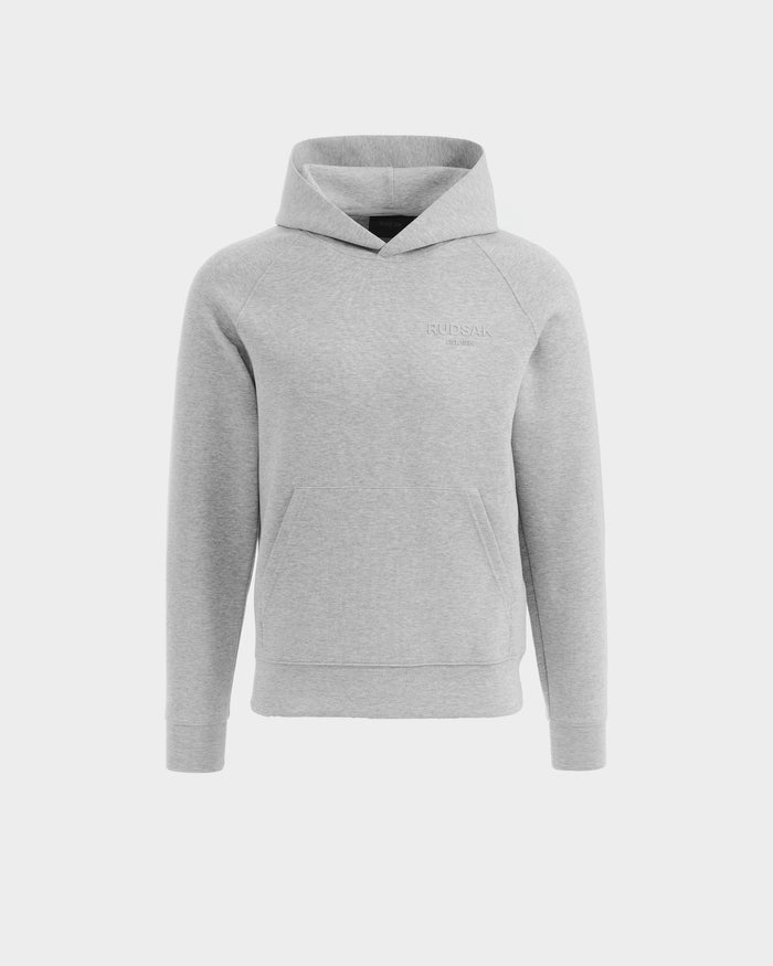The Rudsak BRIAR - 9525001 hoodie in heather grey (size M) is a unisex cotton-blend piece with long sleeves, a front kangaroo pocket, and subtle RUDSAK text on the left chest, shown on a plain white background.