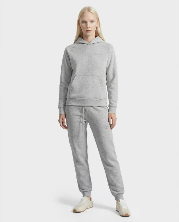 A woman faces forward in a Rudsak BRIAR - 9525001 Heather Grey W cotton-blend hoodie and matching jogger sweatpants with white sneakers, posing against a plain white background.