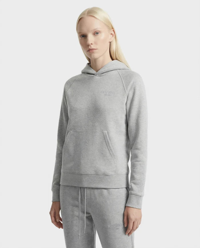 A woman with long blonde hair wears the Rudsak BRIAR - 9525001 Heather Grey W hoodie and matching sweatpants, made from a premium cotton blend, standing against a plain white background.