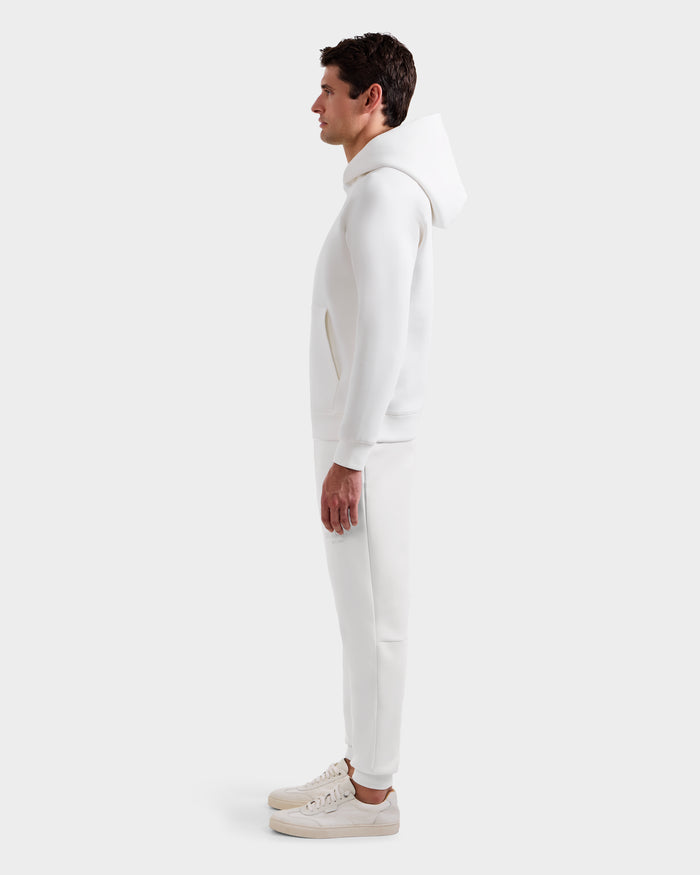 A man in profile wears the Rudsak BRIAR - 9525001 Iceland M, an all-white premium cotton blend unisex hoodie and jogger set, paired with sneakers, posed against a plain light background.