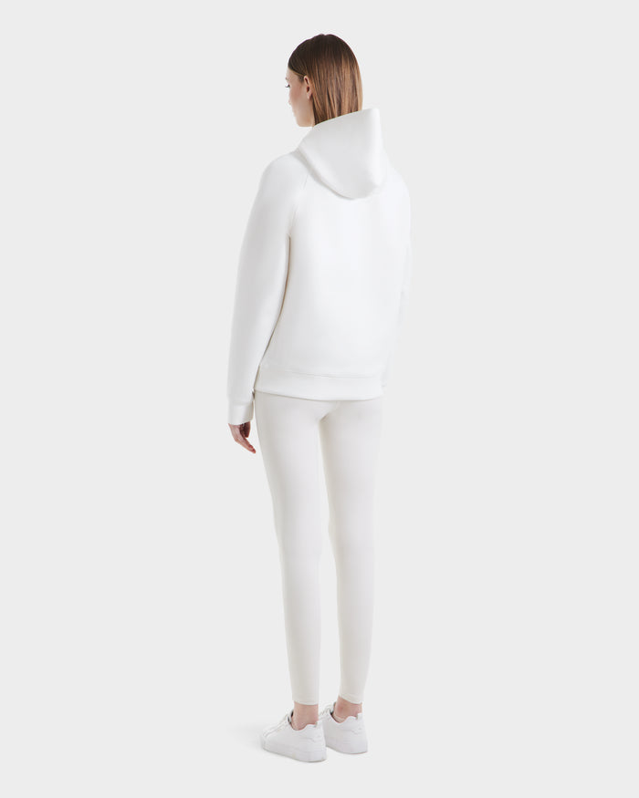 A person stands facing away, dressed in the Rudsak BRIAR - 9525001 Iceland W unisex hoodie made from a premium cotton blend, paired with fitted pants and white sneakers, set against a plain light gray background.