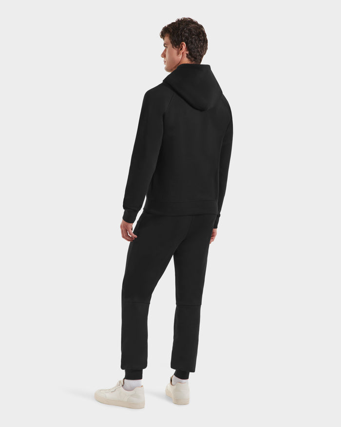 A person stands facing away, wearing Rudsak’s BROOKLYN - 6525593 Black hoodie and black joggers with white sneakers against a plain white background—ideal for a sleek urban style.