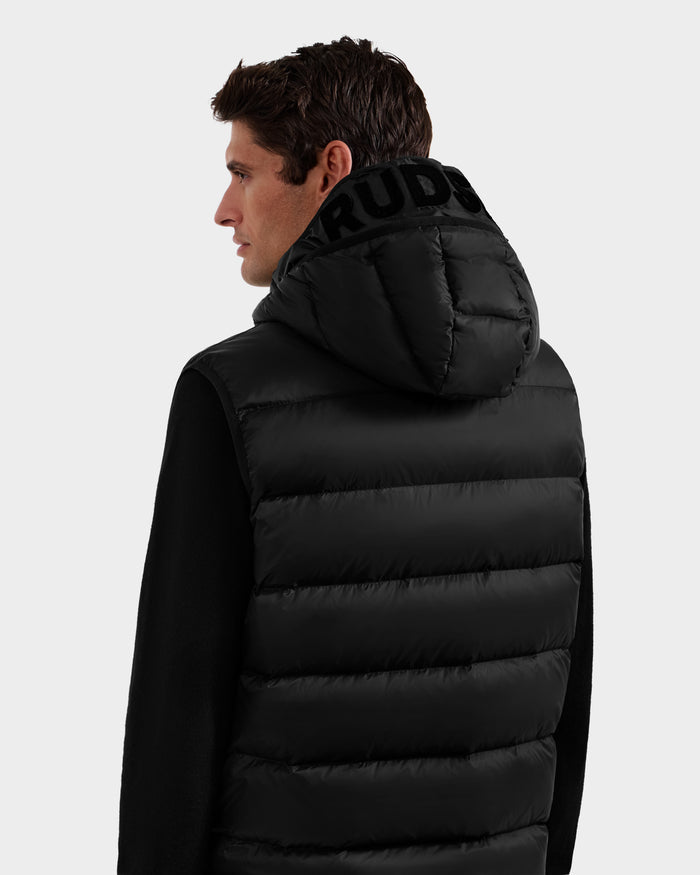 A man with short brown hair is shown from the back, wearing the Rudsak BROOKS - M125520 Black hooded down vest made from recycled nylon, with bold black text on the hood against a plain light gray background.