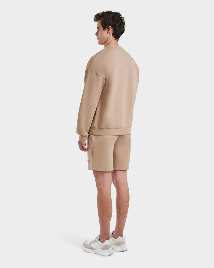 A man stands facing away, wearing the Rudsak BRYN - 9524007 Almond M crewneck sweatshirt and matching shorts with white sneakers, set against a plain white background.