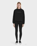 Model faces forward wearing the Rudsak BRYN - 9524007 Black W cotton crewneck sweatshirt with logo, paired with black everyday fit leggings and black sneakers with white soles, set against a plain white background.