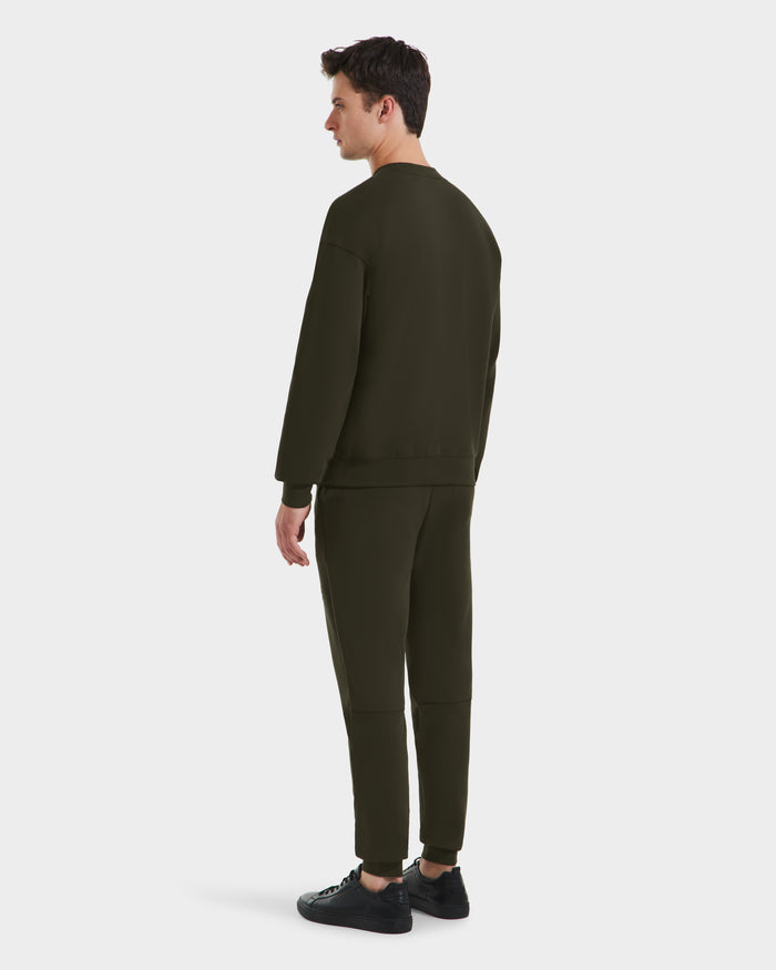 A man stands facing away, wearing Rudsak’s BRYN - 9524007 dark olive crewneck and matching pants in size M, featuring a genderless fit and paired with black sneakers against a plain white background.