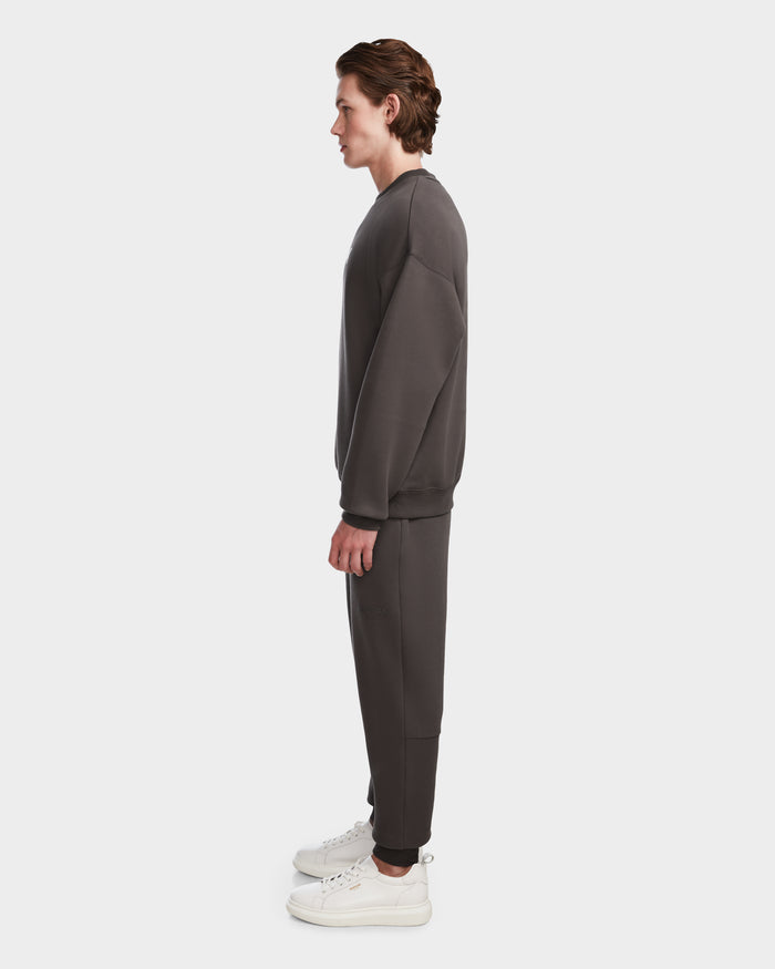 A man in profile wears the Rudsak BRYN - 9524007 Grey M cotton crewneck sweatshirt and sweatpants with white sneakers, highlighting the timeless design against a plain white background.