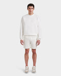 A man faces forward in the Rudsak BRYN - 9524007 Iceland M cotton crewneck sweatshirt with embossed branding, matching shorts, and sneakers. The all-white, genderless outfit delivers an everyday fit against a plain white background.