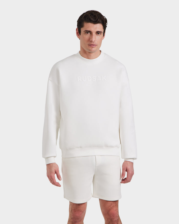 A man stands against a white background wearing the BRYN - 9524007 Iceland M cotton crewneck sweatshirt by Rudsak with a subtle embossed logo and matching white genderless shorts.