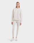A woman with straight blonde hair models the Rudsak BRYN - 9524007 Vanilla W off-white cotton crewneck sweatshirt with embossed detail, paired with matching leggings and white sneakers, against a plain light background.