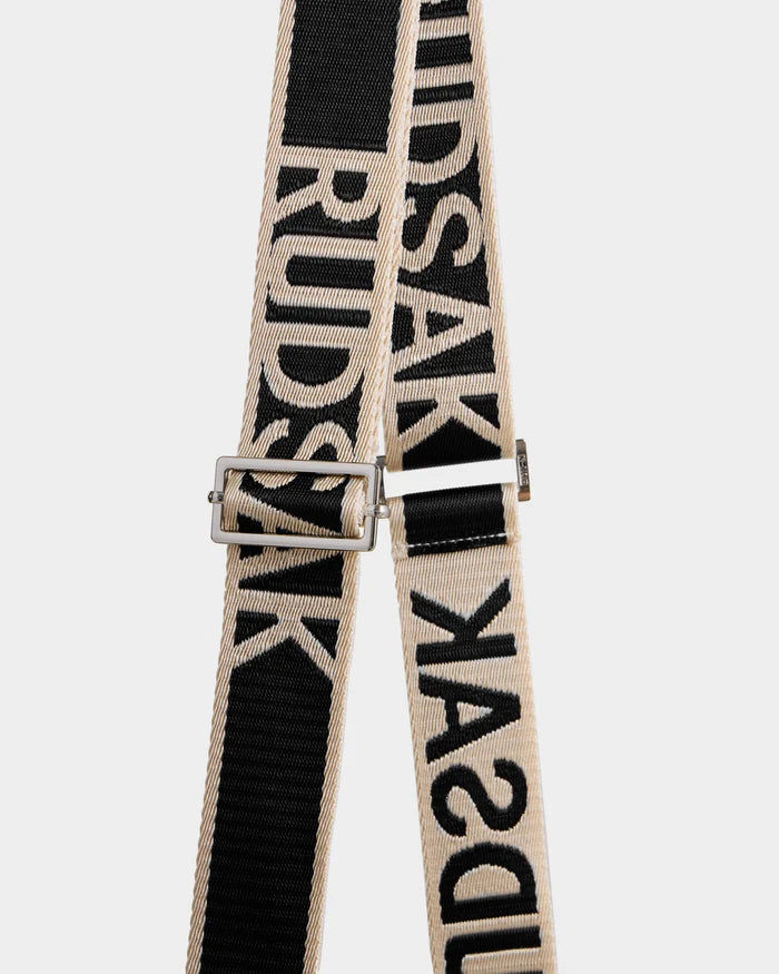Close-up of the Rudsak CABAS - 8325545 Black’s black and beige strap with bold "RUDSAK" lettering and a silver adjustable buckle—an eye-catching accessory that elevates any faux fur mini tote, pictured on a plain white background.