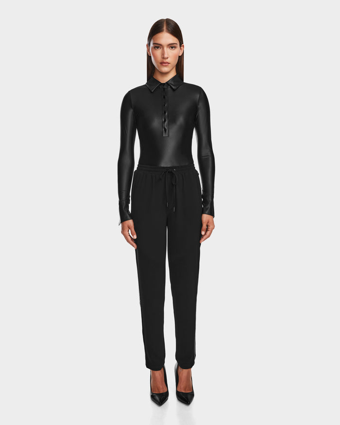 A woman stands facing forward in a black, long-sleeve collared shirt and Rudsak CARDI - 8524561 Black pull-on trousers with black pointed heels, set against a plain white background.