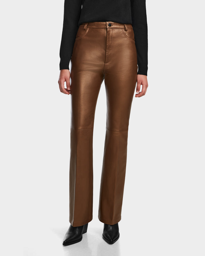 A person stands against a white background wearing Rudsaks CARISSA - 8524545 Antique Bronze high-waisted, straight-leg women’s leather pants, paired with a black long-sleeve top and black pointed-toe shoes.
