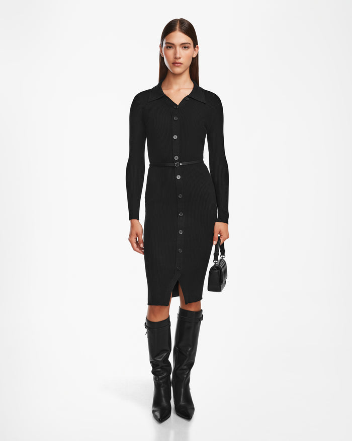 A woman poses against a white background wearing the Rudsak CARLI - 8524573 Black knit dress with a collar, vegan leather belt, knee-high black boots, and holding a small black handbag.